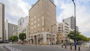 Un hotel de varios pisos con una entrada destacada en esquina, un cartel visible del hotel y una calle con zona de estacionamiento para bicicletas.