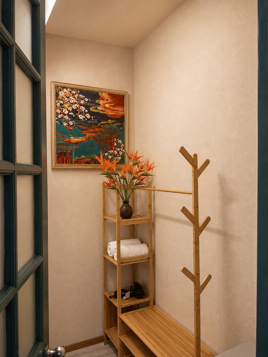 A corner of a room with a wooden shelf holding towels and a vase with flowers, a coat rack, and a painting on the wall.