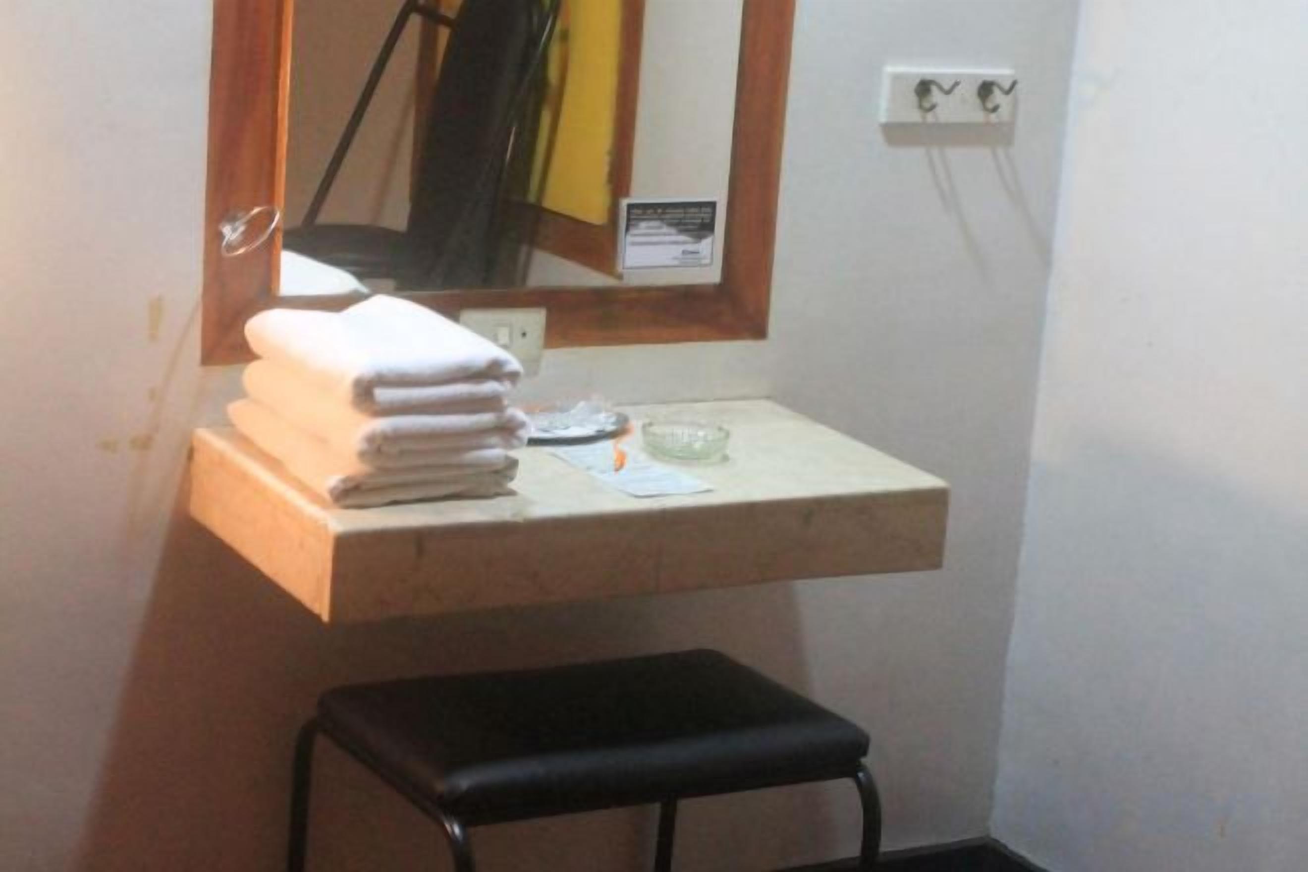 A bathroom with a sink, a mirror, a towel stack, and a black stool.