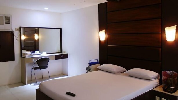 A modern hotel room with a bed, a desk, a chair, a mirror, and wall-mounted lights. - Halina Drive Inn Hotel - Pasay (Pasay)