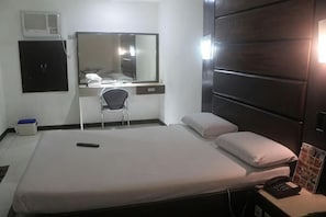 A hotel room with a bed, a desk with a chair, a mirror, a TV, and a bedside table with a phone. - Halina Drive Inn Hotel - Pasay (Pasay)