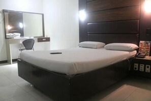 Ein ordentlich bezogenes Bett mit Kopfteil, ein Nachttisch mit Lampe und ein Stuhl.