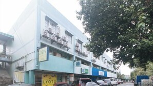 A street view with a row of parked cars and a building with multiple floors and balconies.