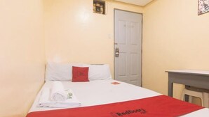 A hotel room with a bed, a red blanket, a white pillow, and a small window.