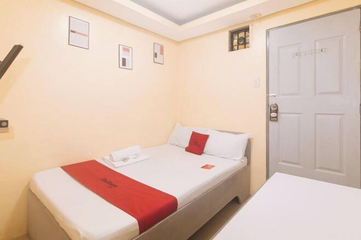Een hotelkamer met een enkel bed, een witte deur en een klein raam.