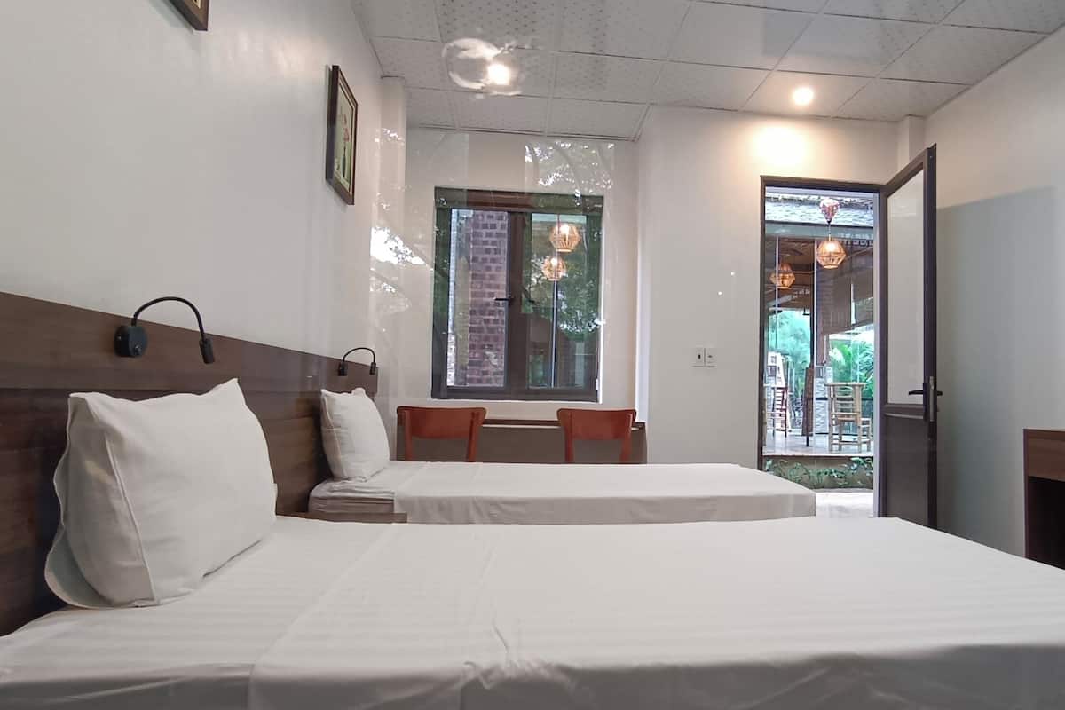 A hotel room with two beds, a wooden headboard, a small table, and a view of the outside balcony.