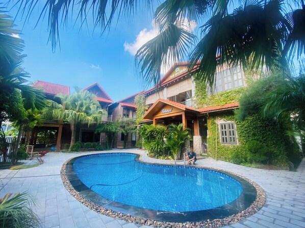 A swimming pool surrounded by a patio area with palm trees and a building with a red roof. - Tam Coc Little Charm Villa & Bungalow (Nam Hoa Lu)