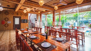 A restaurant with wooden furniture, bamboo ceiling, and large windows overlooking a pool. - Tam Coc Little Charm Villa & Bungalow (Nam Hoa Lu)