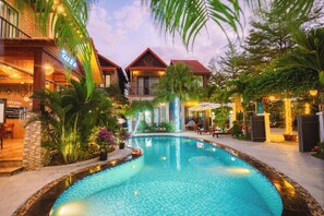 A swimming pool with a tiled edge, surrounded by lush greenery and a building with a red roof. - Tam Coc Little Charm Villa & Bungalow (Hoa Lu)