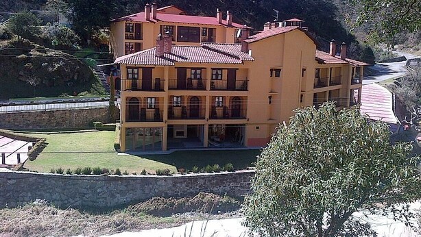 Un edificio a più piani con balconi, un muro di sostegno in pietra e una zona pavimentata di fronte.