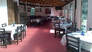 Un'ampia sala da pranzo con diversi tavoli e sedie, travi in legno a soffitto e ampie finestre che lasciano entrare la luce naturale.