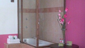 Un bagno con doccia vetrata, una vasca da bagno, un tavolino con articoli da toilette e un vaso con fiori.