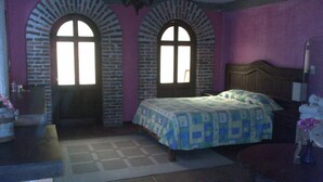 Una camera da letto con un letto, due finestre ad arco, un lampadario e un bagno con un lavandino e uno specchio.