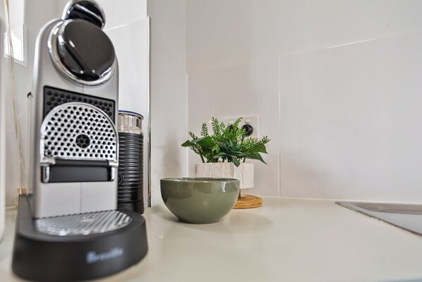 A coffee machine, a green bowl, and a potted plant on a white countertop. - Cairns Tropical Bliss Swim In - Out Apt (Cairns North)