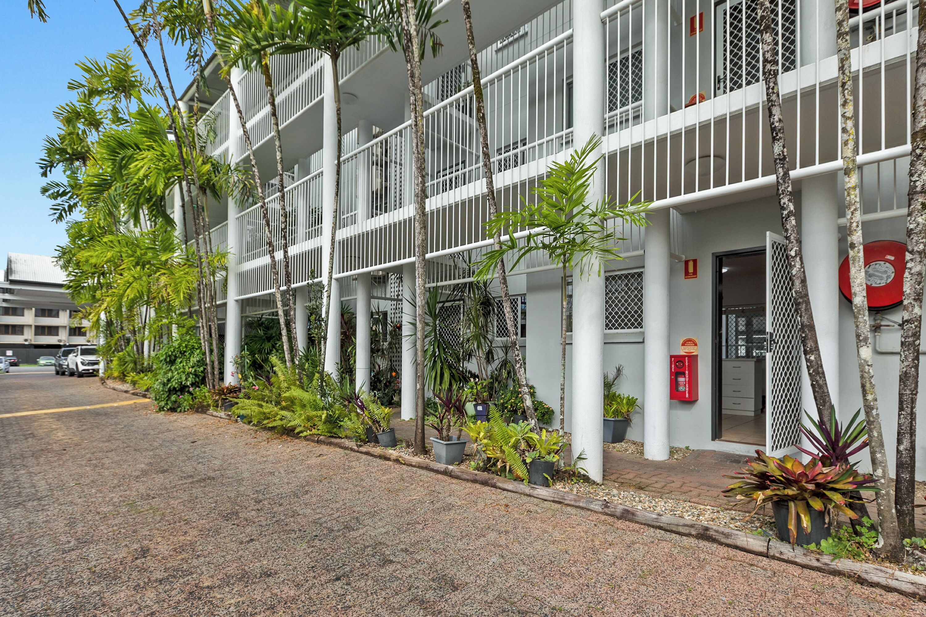 Un edificio de varios pisos con balcones, plantas en macetas y un buzón rojo.