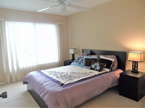 A bedroom with a bed, two bedside tables, a ceiling fan, and a window with curtains.