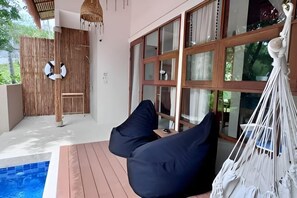 Una habitación moderna con piso de madera, un ventanal con cortinas, una hamaca y una piscina pequeña.