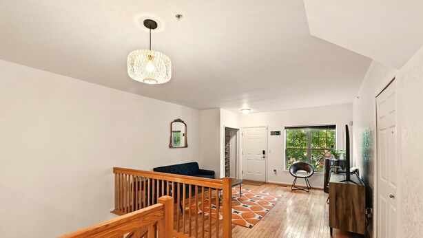 A spacious hallway with wooden flooring, a staircase with a wooden railing, a large window with a view of greenery, and a modern pendant light fixture.
