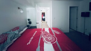 A bedroom with a bed, a door leading to a hallway, and a television on the wall.