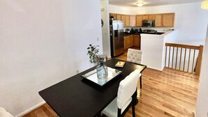 A modern kitchen with wooden cabinets, stainless steel appliances, and a dining area with a black table and white chairs.