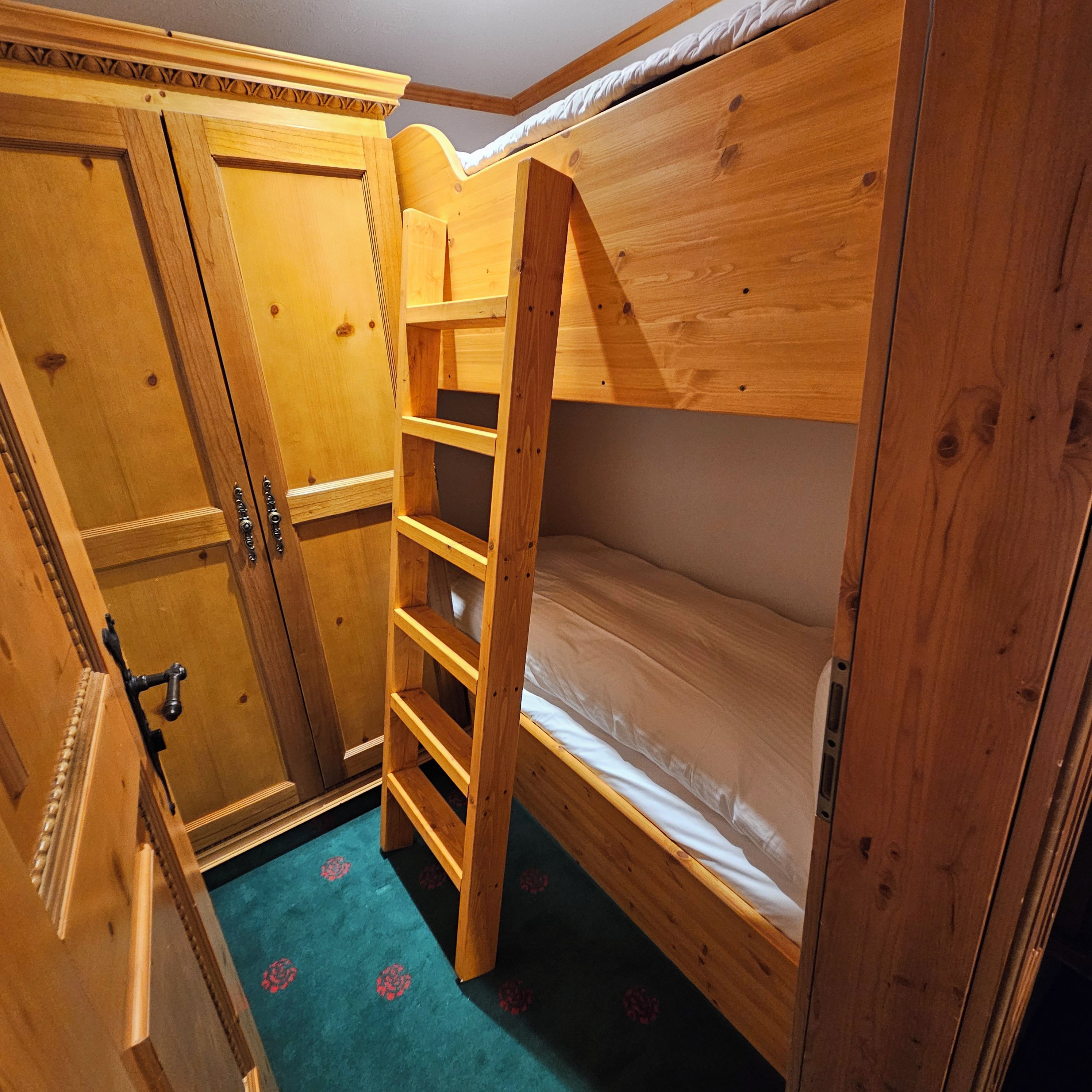 A bunk bed with a wooden ladder and a wardrobe with a mirror.