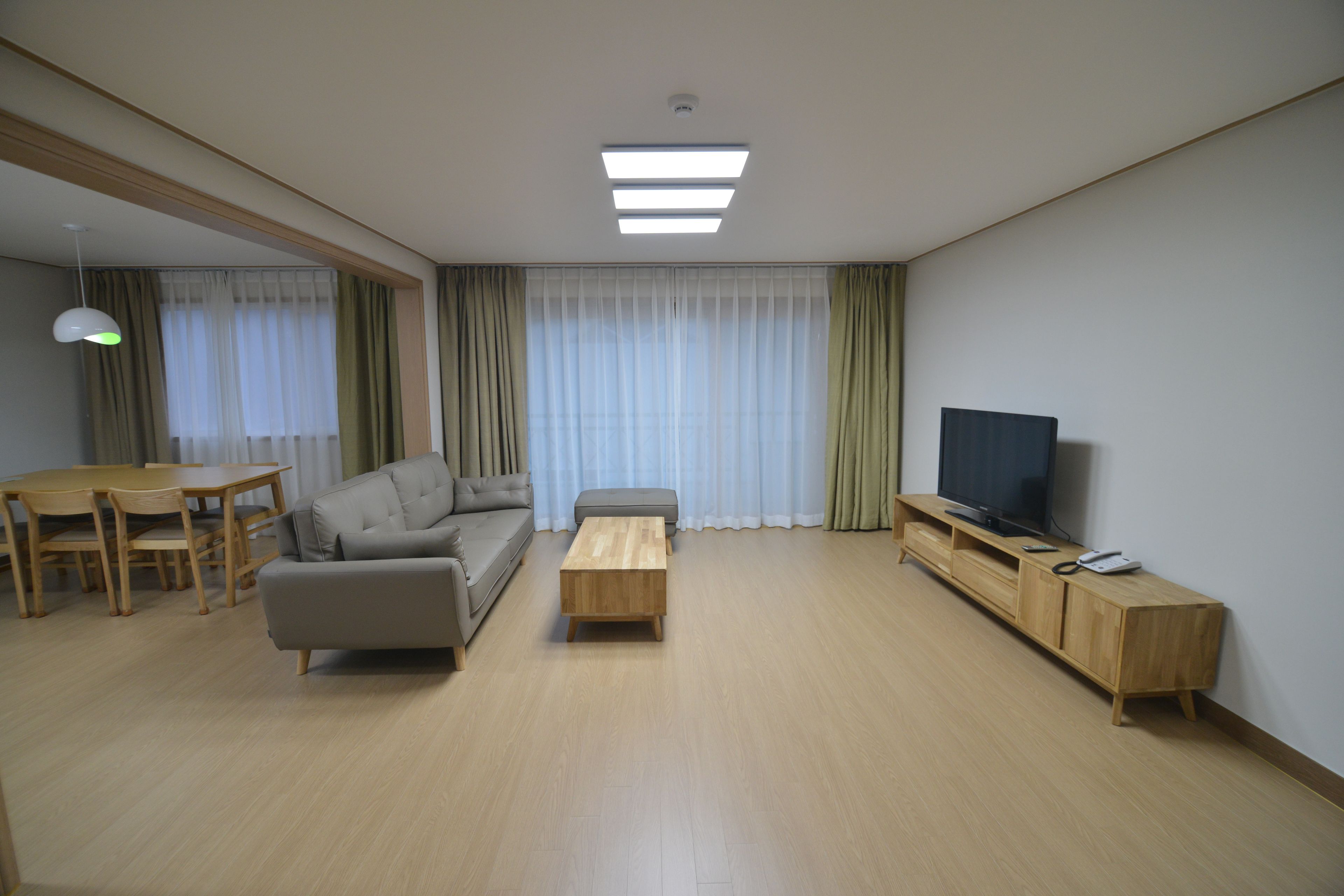 A modern living room with a sofa, coffee table, TV stand, and dining area.