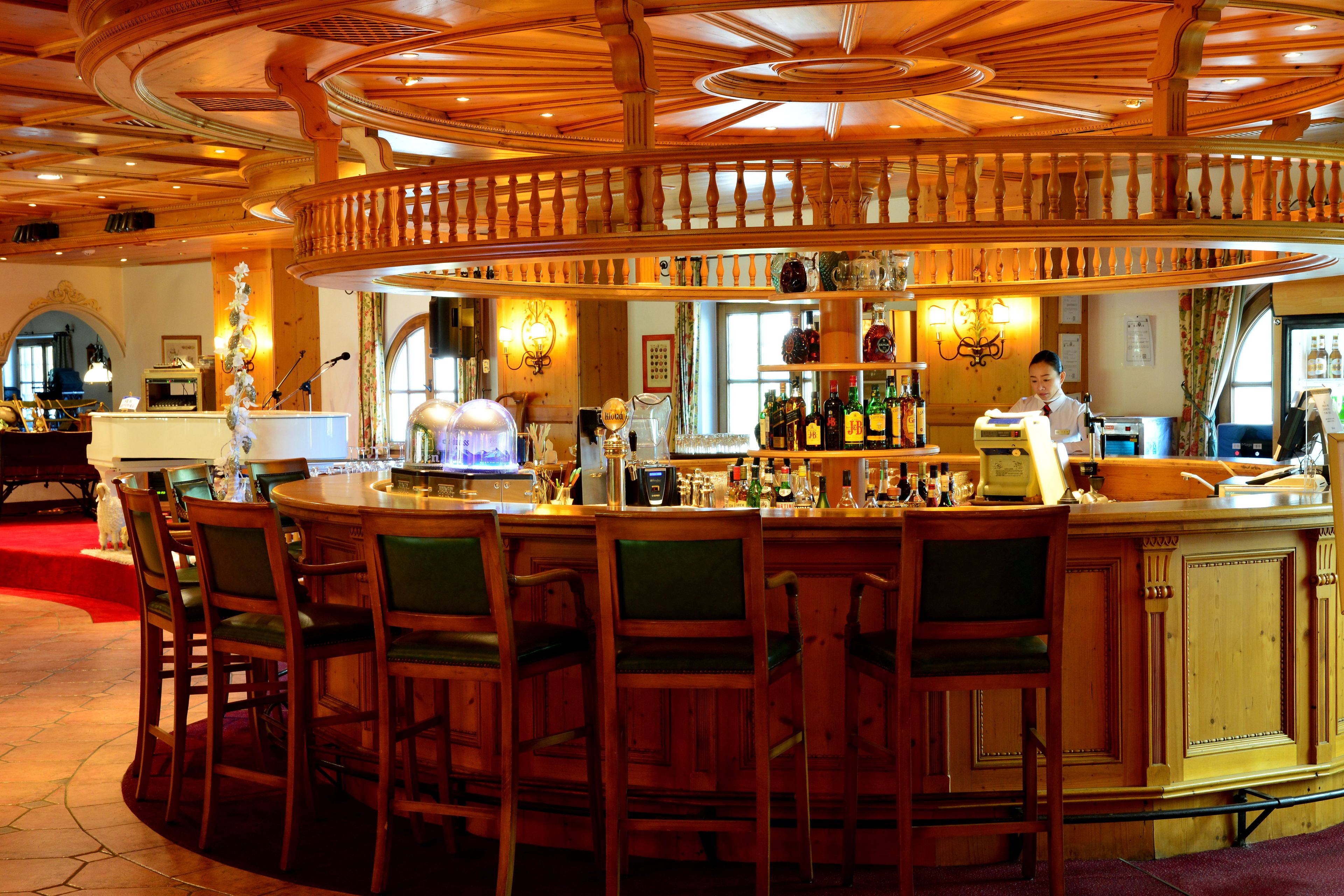 Zona de bar con muebles de madera, un barman y varias botellas.