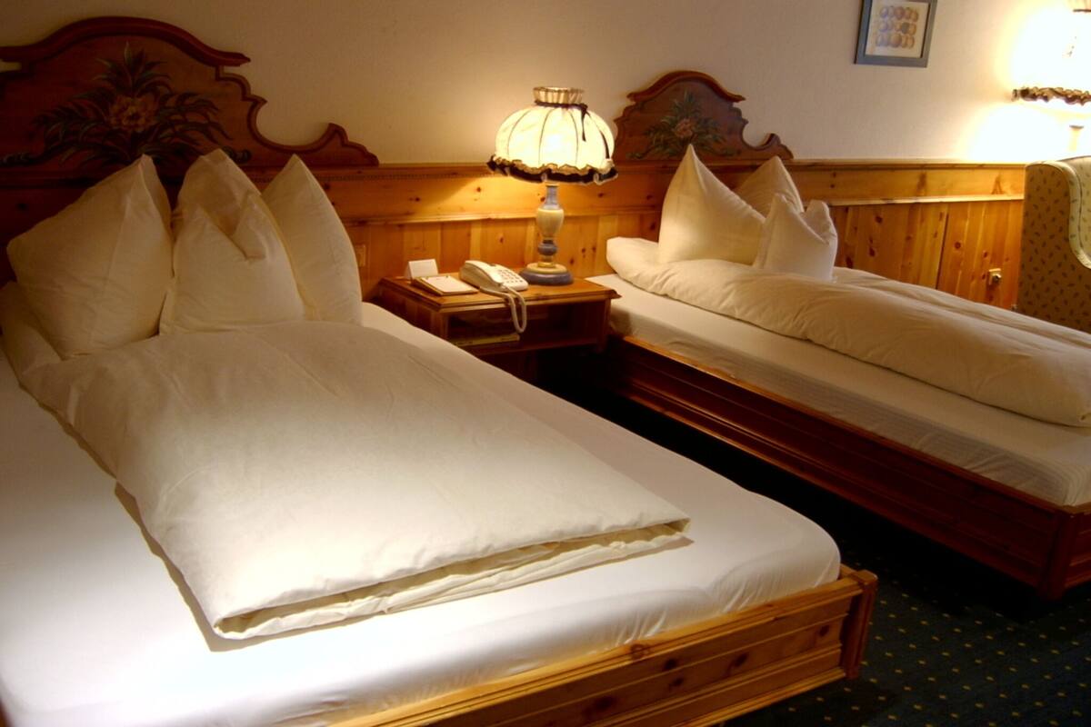 Une chambre d’hôtel avec deux lits simples, une tête de lit en bois, une table de chevet avec une lampe et un téléphone.