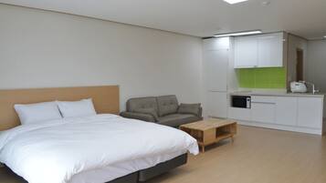 A modern hotel room with a large bed, a sofa, a wooden coffee table, and a kitchenette area.
