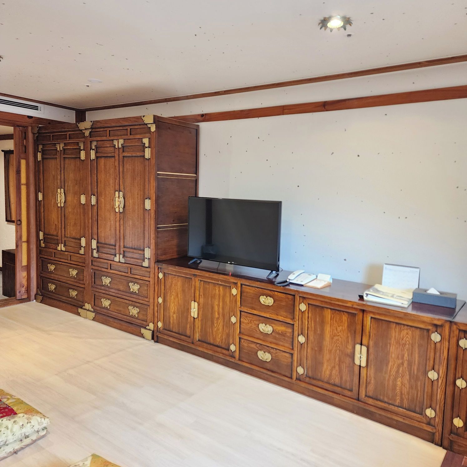 Una habitación con un armario de madera, un televisor y un escritorio con un teléfono y papeles.