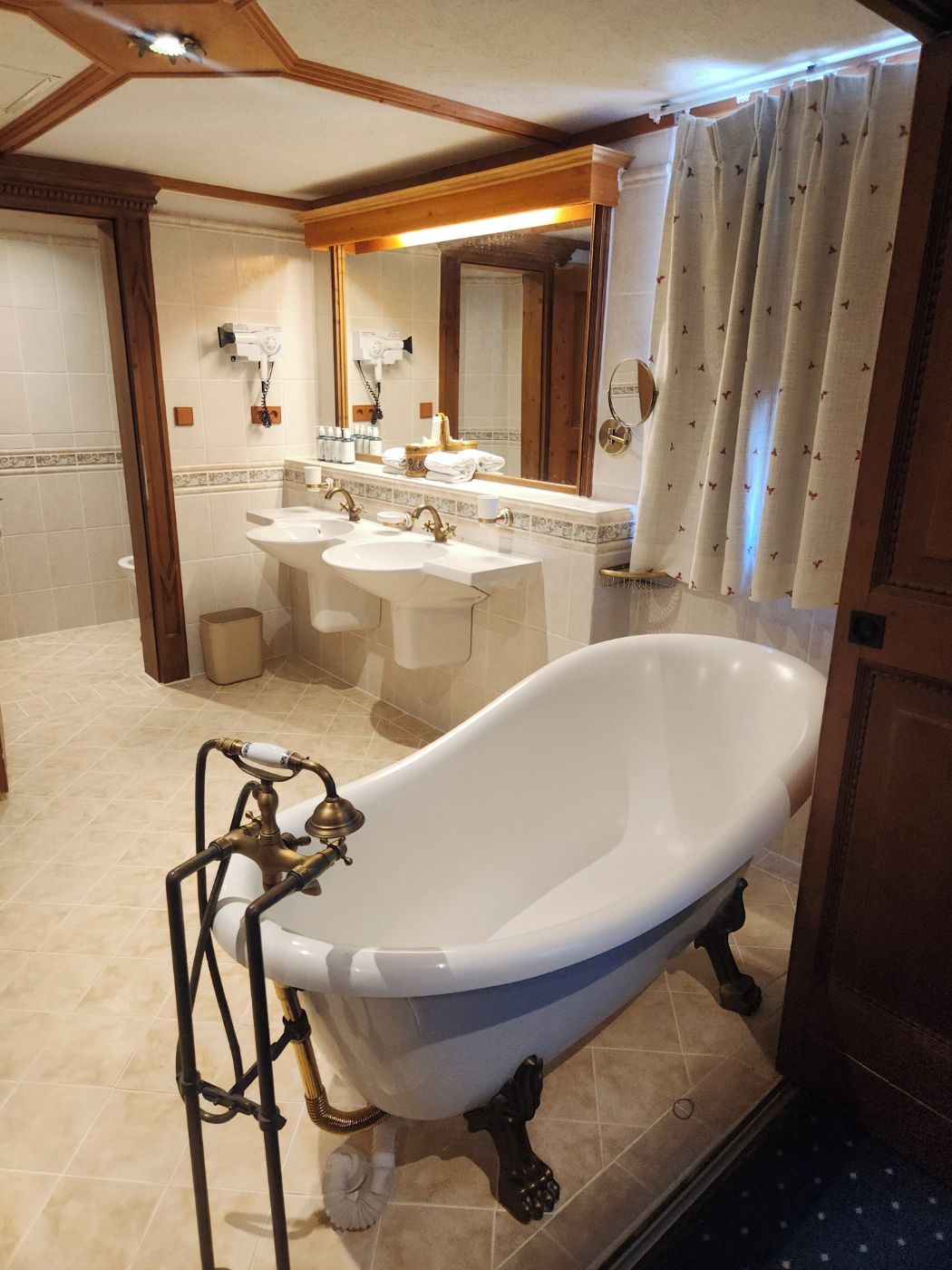 A bathroom with a freestanding bathtub, two sinks, a mirror, and a shower curtain.