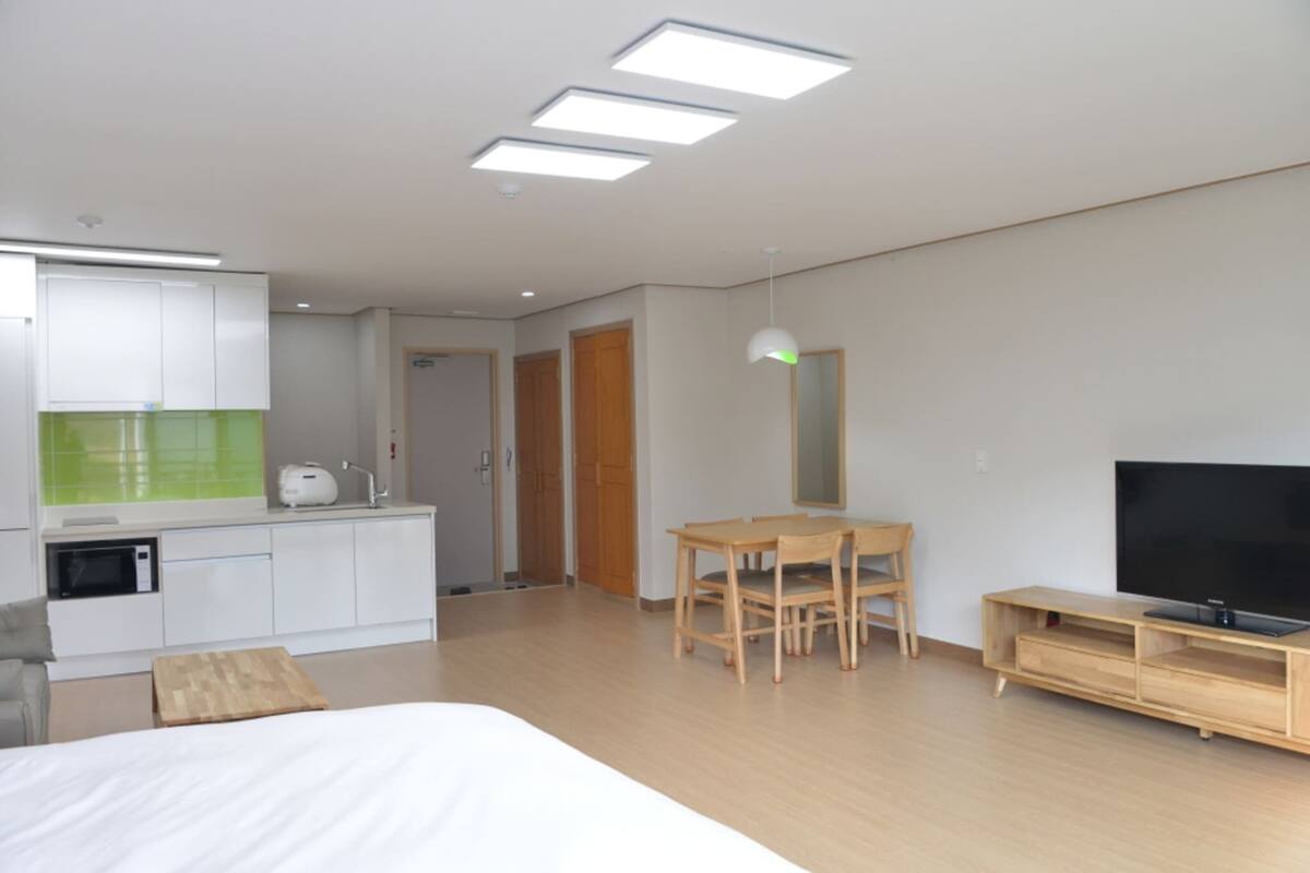Une chambre d’hôtel moderne comprenant un lit, une table à manger avec des chaises, un téléviseur, un coin cuisine avec un four à micro-ondes et un meuble en bois.