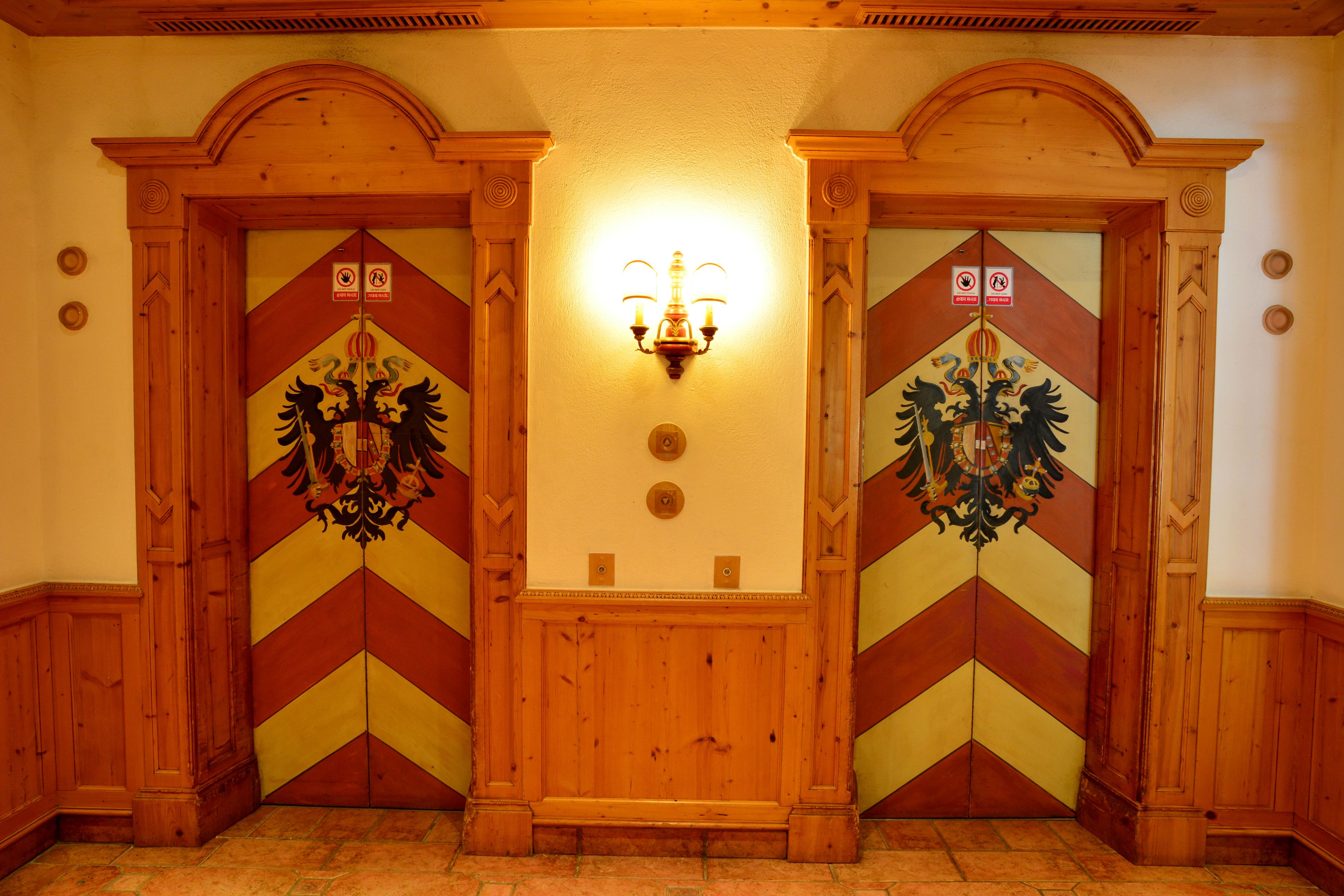 Un couloir avec deux portes en bois, chacune ornée d’un motif décoratif et surmontée d’un luminaire.