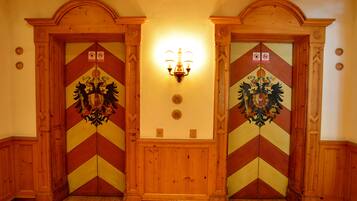 Un couloir avec deux portes en bois, chacune ornée d’un motif décoratif et surmontée d’un luminaire.
