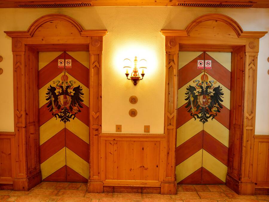Un couloir avec deux portes en bois, chacune ornée d’un motif décoratif et surmontée d’un luminaire.