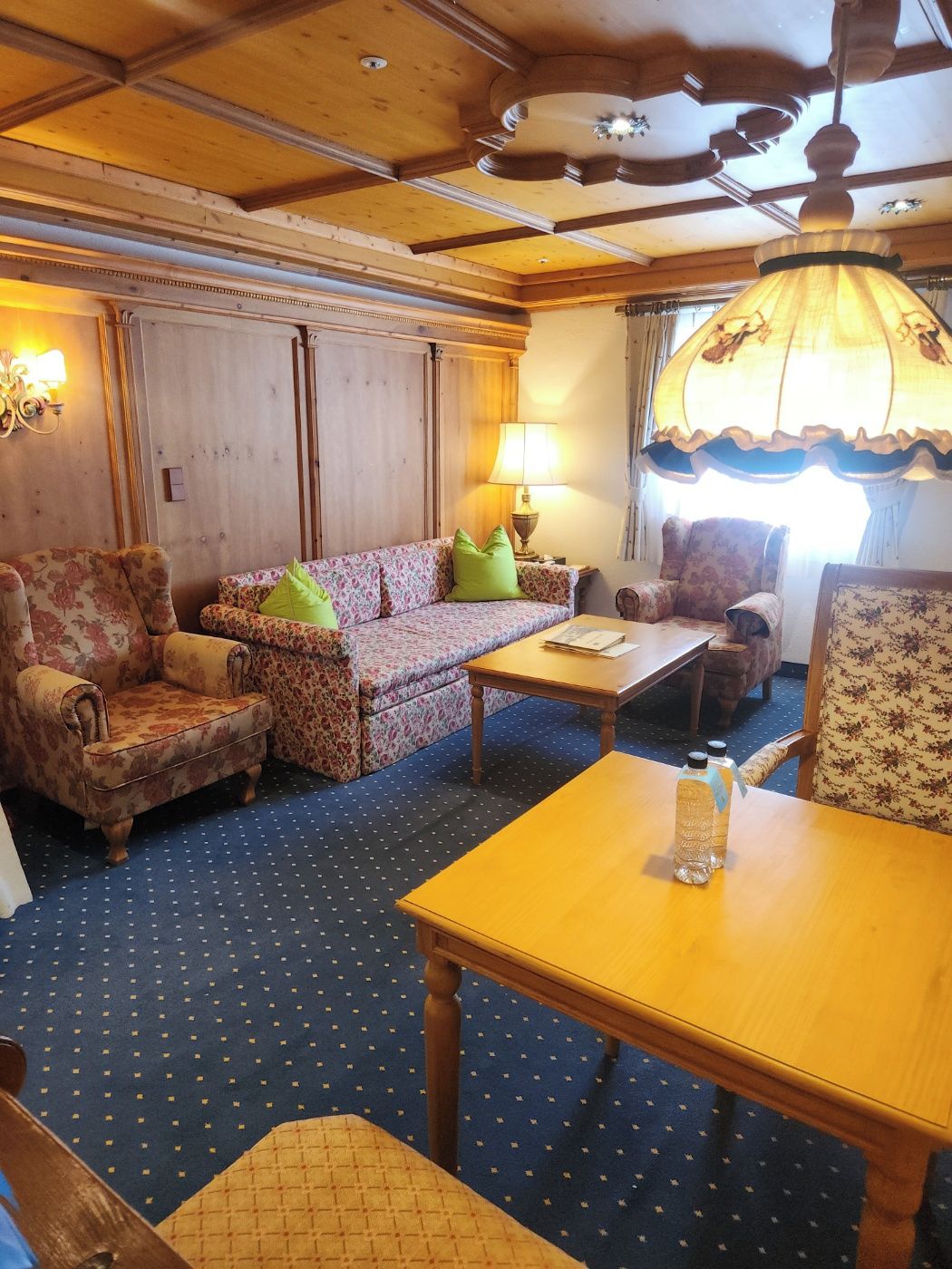 A room with a wooden ceiling, floral-patterned sofas, a wooden table, and a patterned carpet.