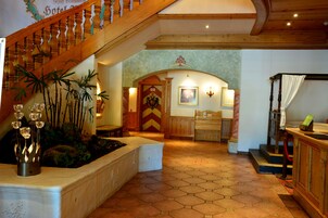 A hotel lobby with a wooden staircase, a reception desk, and a decorative plant arrangement.
