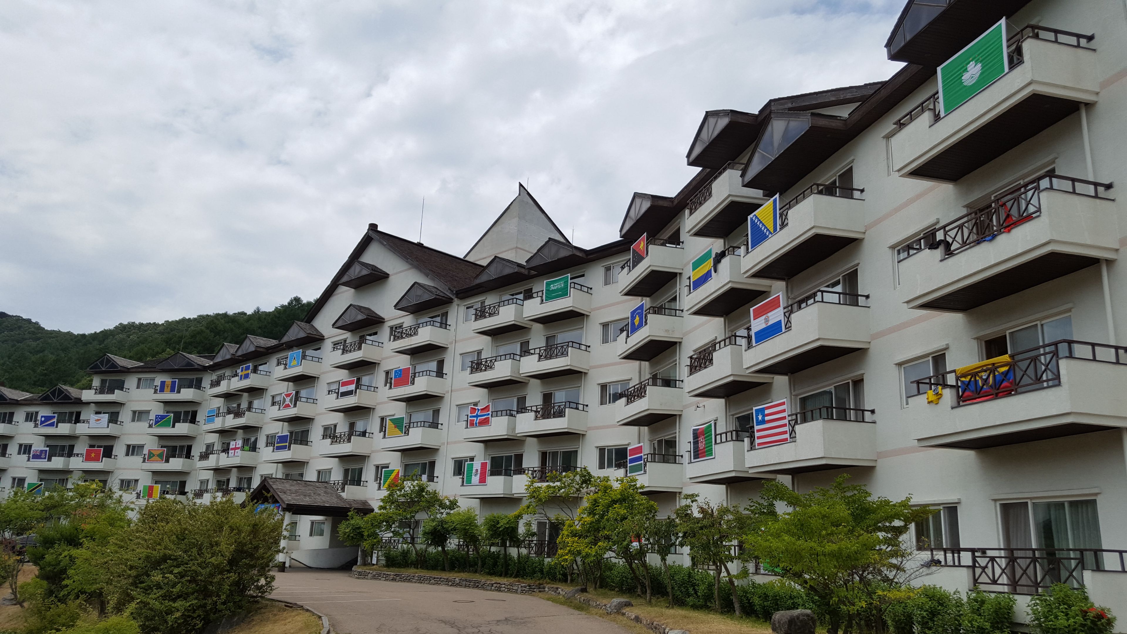 A multi-story hotel with balconies, flags, and a mountainous backdrop.