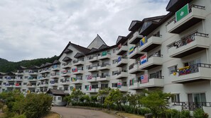 A multi-story hotel with balconies, flags, and a mountainous backdrop. - Muju Deogyusan Resort (Muju)