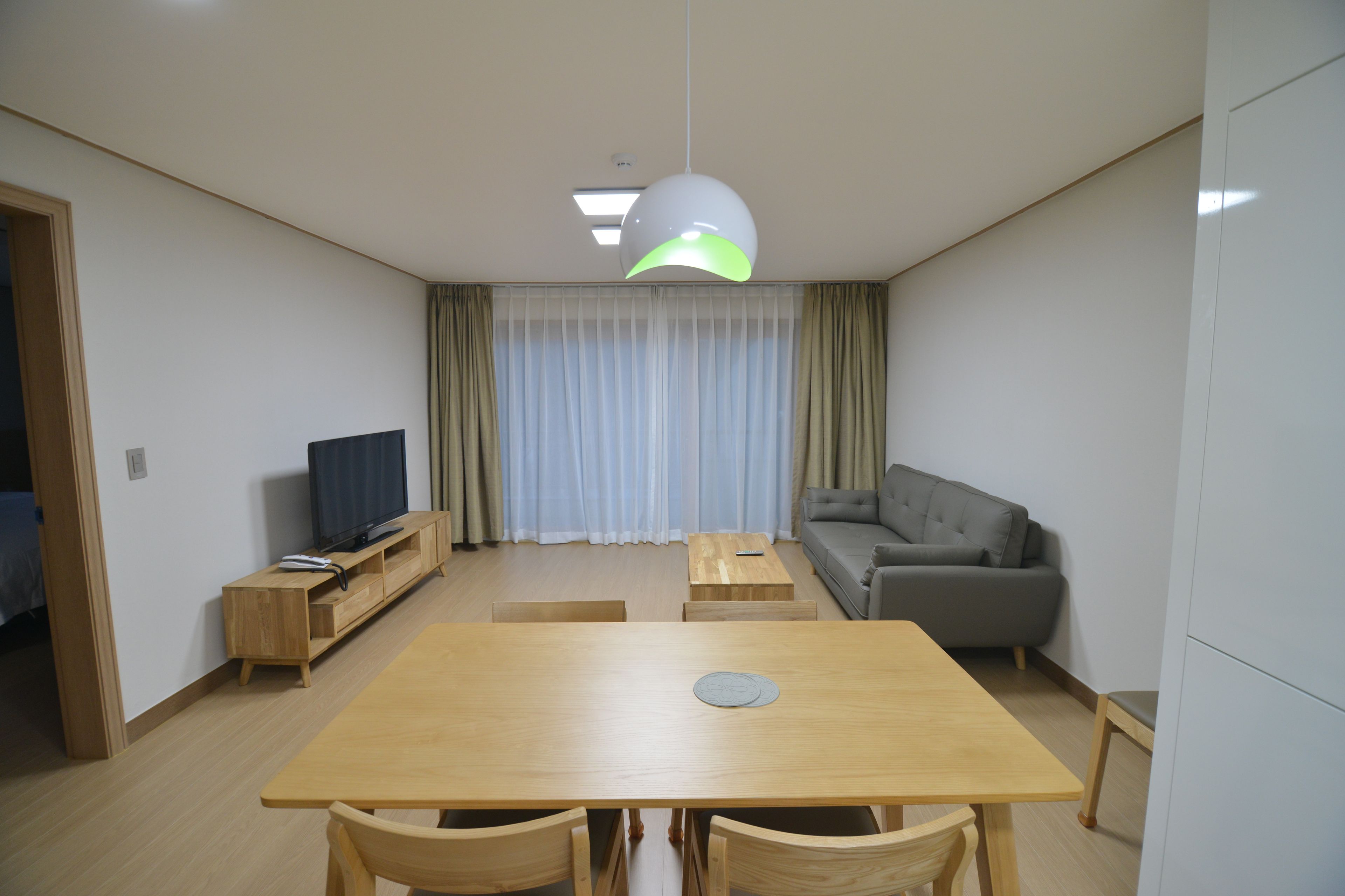 Uma sala de estar moderna com uma mesa de jantar de madeira, um sofá cinza e uma televisão sobre um suporte de madeira.