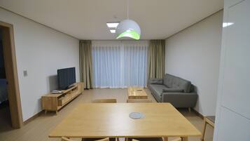Uma sala de estar moderna com uma mesa de jantar de madeira, um sofá cinza e uma televisão sobre um suporte de madeira.