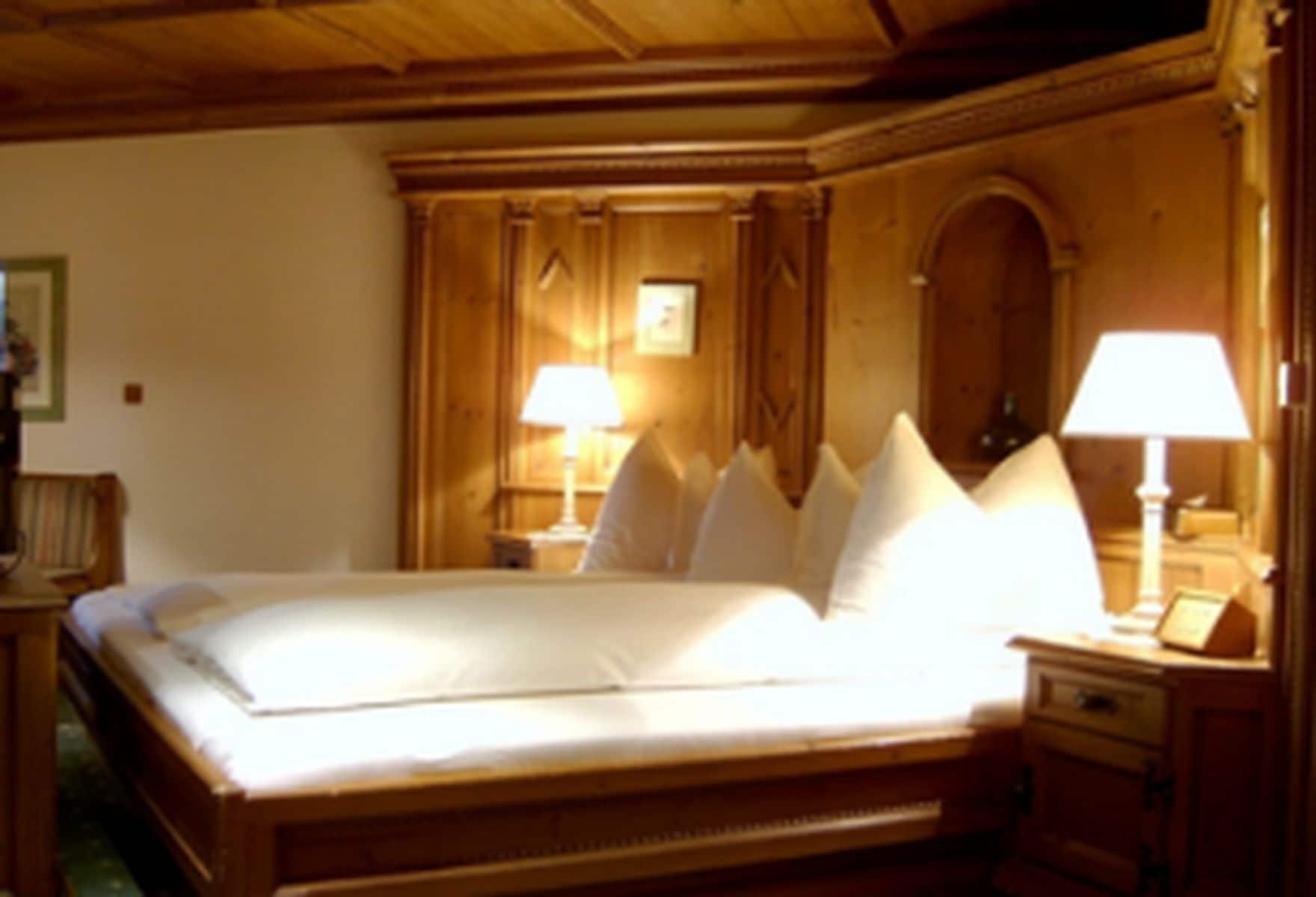 A hotel room with a large bed, wooden headboard, two bedside tables with lamps, and a wooden wardrobe.