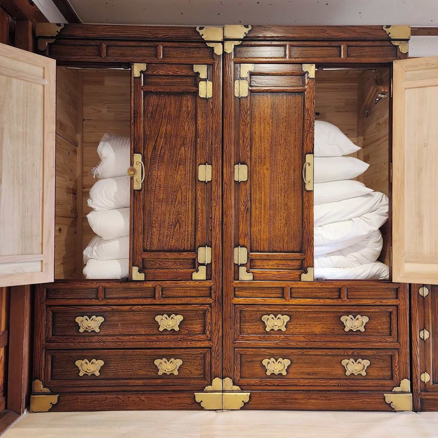 A wooden wardrobe with multiple drawers and a central door, featuring brass handles and hinges.