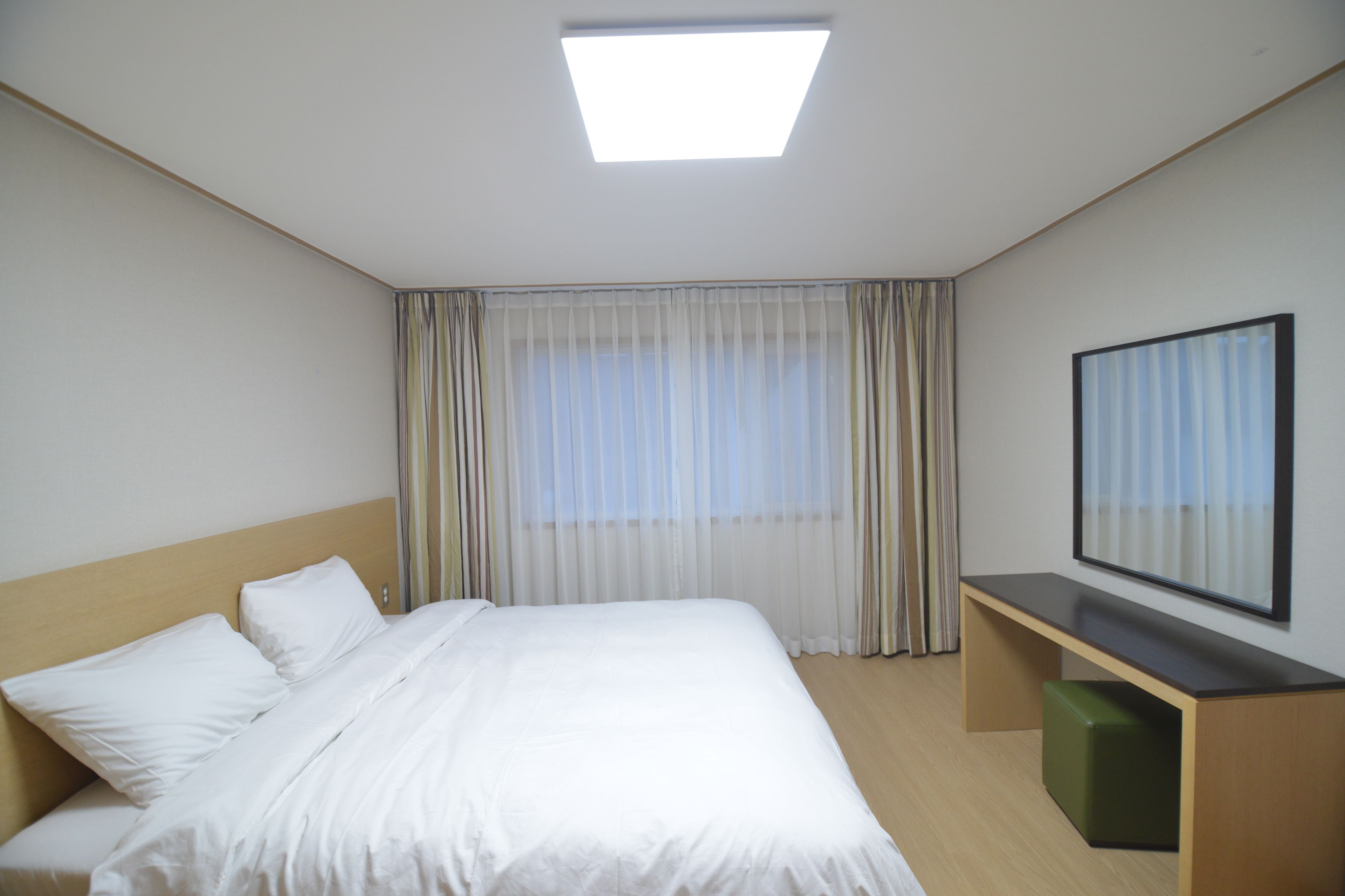 A hotel room with a bed, a desk, a chair, a window with curtains, and a ceiling light.