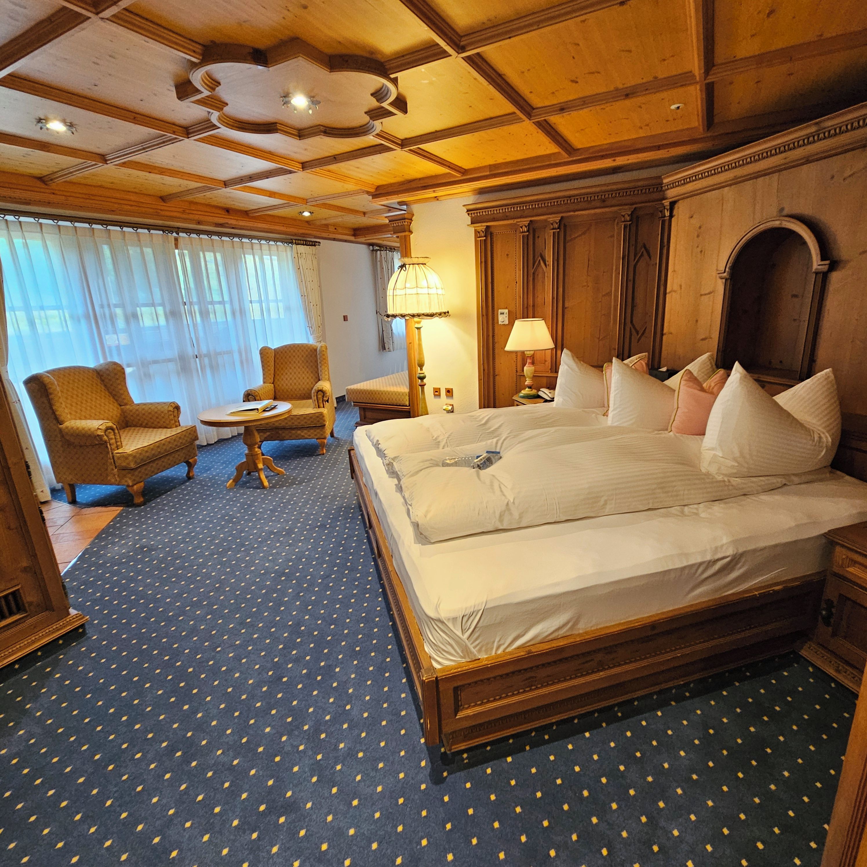 Una habitación de hotel con una cama grande, dos sillones, una mesita y una lámpara.