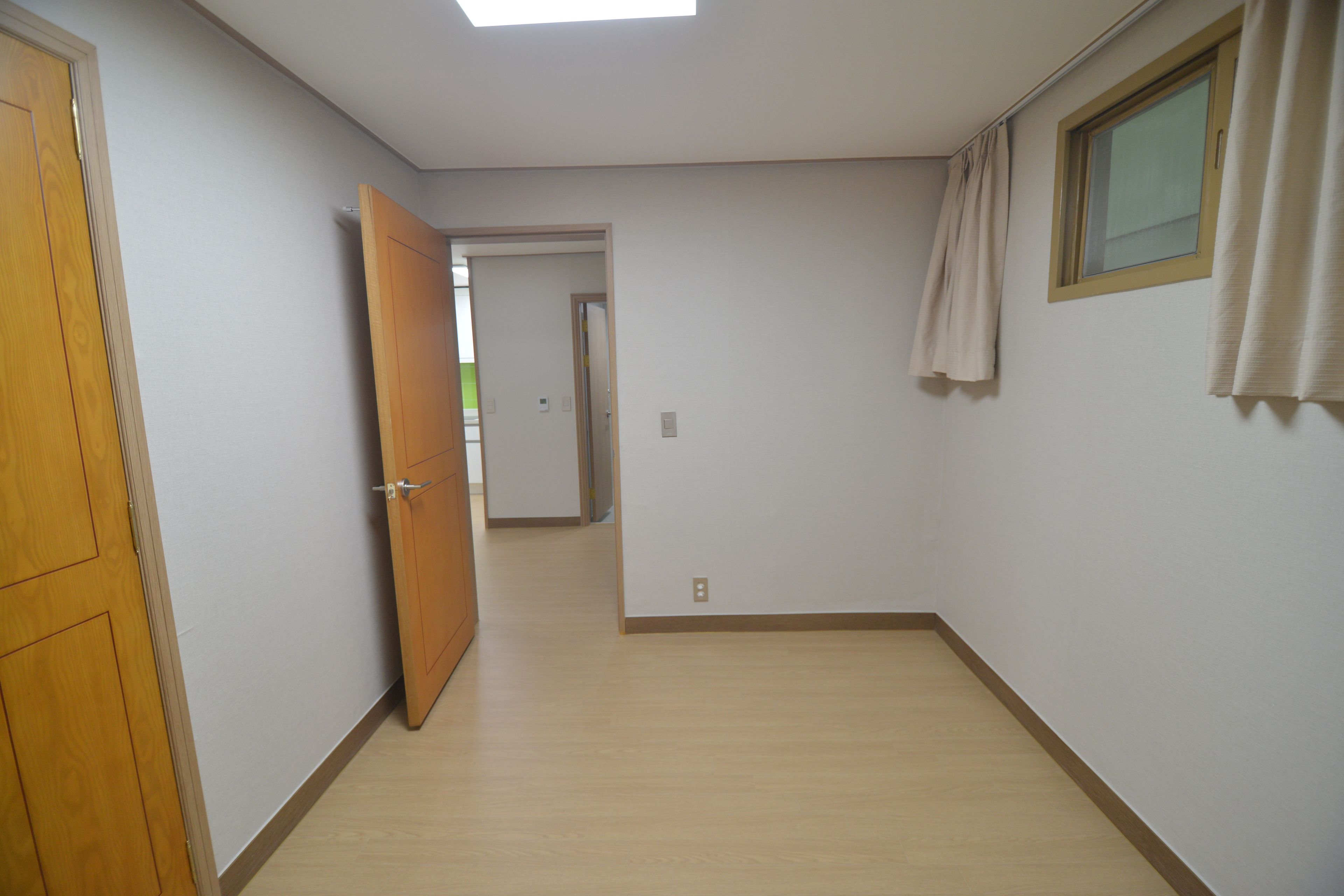 A hallway with wooden doors, a window with curtains, and a light switch on the wall.