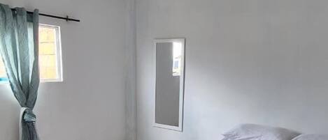 A bedroom with a bed, a window, and a curtain.