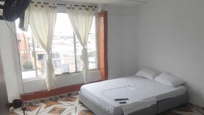 A bedroom with a bed, a window with curtains, a radiator, and patterned floor tiles. - Hospedaje ASL HOME (Yumbo)