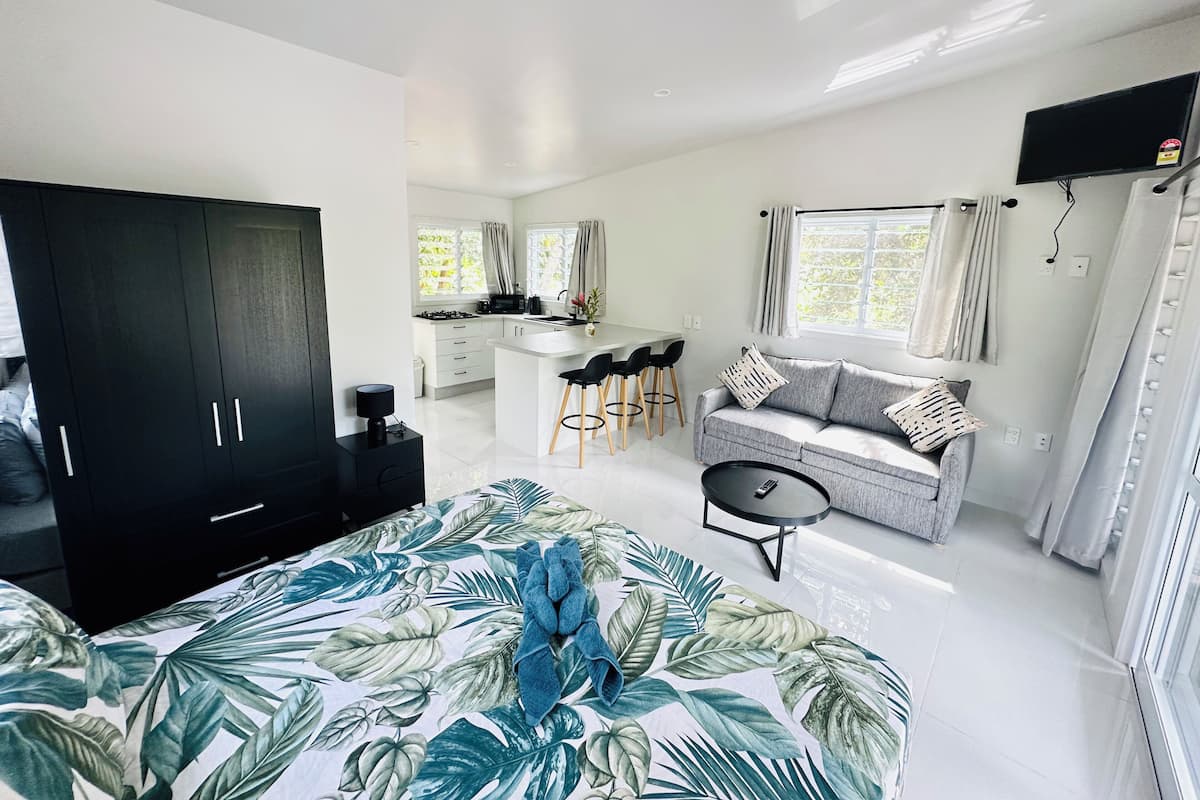 A modern, well-lit bedroom with a large bed, a sofa, and a dining area with bar stools.