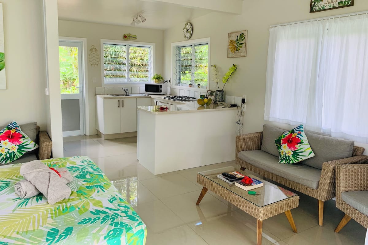 A modern kitchen with white cabinets, a microwave, and a small island. There is a dining area with a sofa and a coffee table.